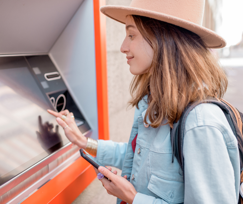 Image of a young woman in a nice hat using a through the wall ATM to complete a banking transaction.